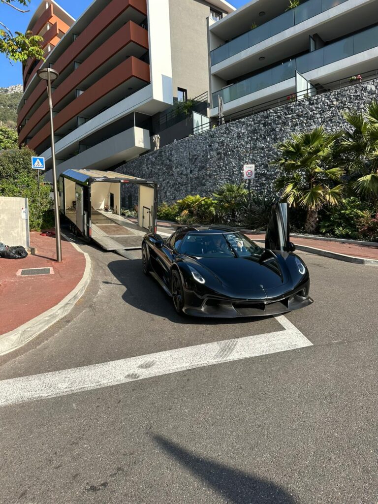 Zwarte hypercar met opengeklapte deur naast de geopende gesloten trailer